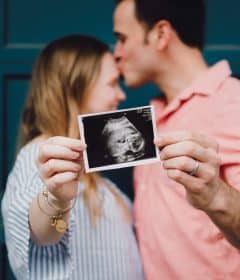 man kissing woman's forehead white holding ultrasound photo